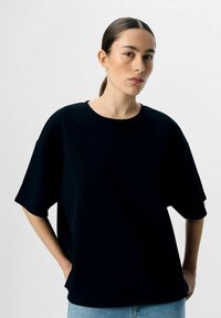 Zwarte oversized t-shirt met een ronde hals, korte mouwen en een gladde textuur. Gekocht met lichtblauwe jeans, minimalistisch ontwerp.