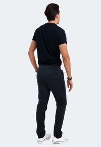 Schwarzes Kurzarmhemd, marineblaue Hose mit Taschen und weiße Sneakers. Die Ansicht zeigt den Rücken und hebt den Schnitt sowie die Materialtexturen hervor.