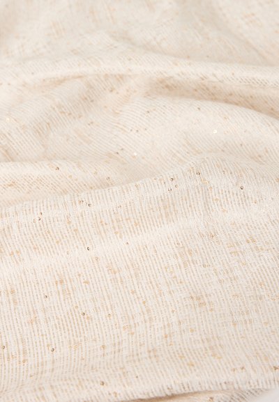 Υφασμα σε κρεμ απόχρωση με μικρές, διάσπαρτες χρυσές παγιέτες και χαλαρό πλεκτό μοτίβο, εμφανιζόμενο σε απαλές πτυχώσεις.