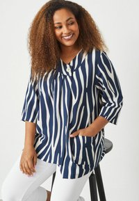 Top a righe blu navy e bianche con maniche corte, dettagli con bottoni e tasche; realizzato in tessuto leggero con una vestibilità ampia.