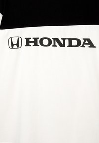 Lyhythihainen mustavalkoinen paita, jossa on "HONDA"-logo paksuilla mustilla kirjaimilla rinnassa ja sileä puuvillapinta.