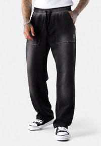 Schwarze Sweatpants mit einem lockeren Schnitt, mit elastischem Bund und Kordelzug. Mit abgetragenen Details und dezentem Markenlogo auf der Vorderseite.
