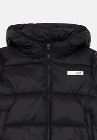 Svart pufferjacka med dragkedja fram, huva och en liten EA7-logotyp. Materialet är glänsande, med ett quiltat mönster och vadderad textur.