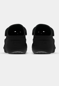 Tamancos de borracha preta com tiras traseiras, apresentando furos de ventilação e uma superfície ligeiramente texturizada; silhueta curva e design leve.