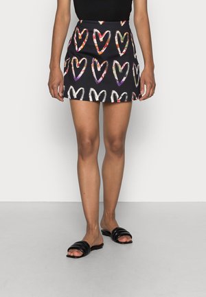 Black mini skirt with colorful heart patterns worn with black slip-on sandals and a black top, showing a front view of legs.