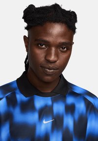 Nike polo shirt met een blauw-zwart verlooppatroon, een zwarte kraag en een klein wit Swoosh-logo op de borst.