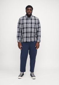 Black and white plaid shirt with long sleeves, button-down collar, worn with navy trousers and black sneakers. Simple design and fitted shape.