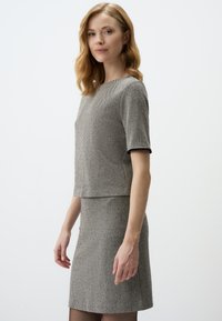 Ensemble deux pièces ajusté gris avec un motif en chevrons texturé. Manches courtes sur le haut ; la jupe tombe au-dessus du genou. Design simple et épuré.