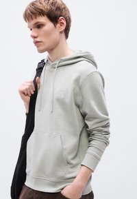 Ανοιχτό γκρι φούτερ με κουκούλα, μπροστινή τσέπη, κορδόνι κουκούλας και μικρό λογότυπο. Μαλακό ύφασμα, άνετη εφαρμογή και ριμπ μανσέτες.