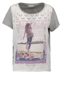 Triko s krátkým rukávem s fotografickým potiskem osoby u vody, s šedým rukávem a dekorativními okraji v odstínech modré a růžové.
