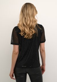 Svart kortärmad topp med paljettdesign och genomskinlig randig textur. Lättviktsmaterial, avslappnad passform och böjd nederkant.