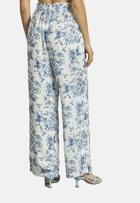 Weite Hose aus weißem Stoff mit blauem Blumenmuster. Elastischer Bund und leichte Textur. Kombiniert mit blauen High Heels.