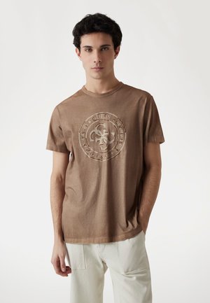 Bruine katoenen t-shirt met een gestructureerd cirkelvormig logo in het midden. Korte mouwen, ronde halslijn en een comfortabele pasvorm. Glad textuur van de stof.