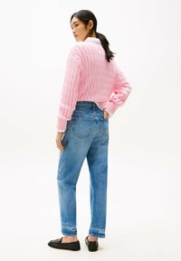 Suéter de punto rosa con patrón texturizado, combinado con unos vaqueros de cintura alta en tono azul claro. Unos zapatos negros tipo slip-on completan el atuendo.