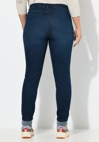 Des jeans skinny en denim bleu foncé dotés d'une ceinture élastique, de deux poches arrière et d'un ourlet retroussé. Portés avec des baskets multicolores.