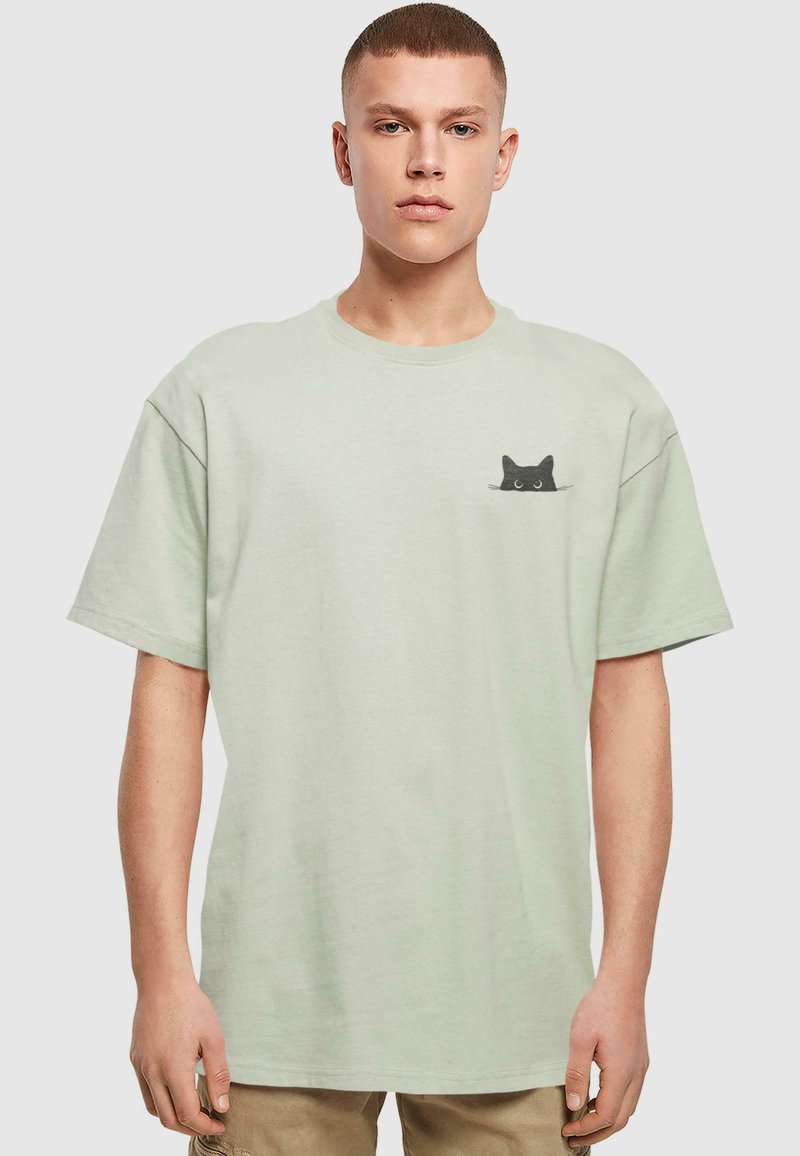 Light green cotton t-shirt with a relaxed fit, featuring a black cat graphic on the left chest. Short sleeves and crew neckline.