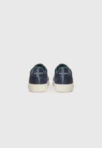 Navy blue suede sneakers with a leather heel tab, white rubber soles, and a green fabric lining. Logo on the heel accent.