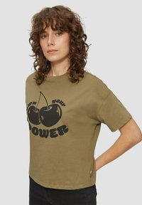 Olijfgroene katoenen t-shirt met een relaxte pasvorm, voorzien van een zwarte kersengrafiek en vetgedrukte tekst waarop "POWER" staat aan de voorkant.