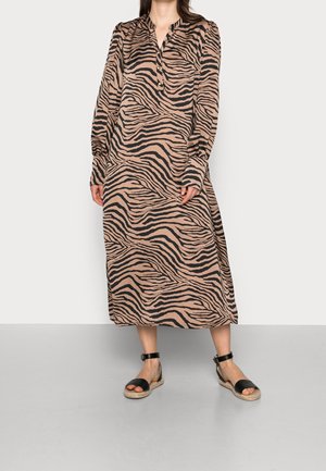 Langes, braunes und beigestreiftes Zebra-Kleid mit Kragen und Knopfdetails, mit langen Ärmeln und lockerer Passform. Getragen mit schwarzen Sandalen.