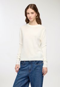 Maglione color crema con scollatura rotonda, maniche lunghe e polsi e orlo a coste; indossato con jeans in denim blu. Texture morbida e leggera.
