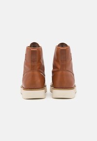 Brown leather ankle boots with a smooth finish, rubber soles, and minimal stitching. The design features a subtle logo on the side.
