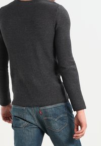 Dunkelgraues langärmeliges Strickoberteil mit strukturierter Oberfläche, kombiniert mit blauen Jeans aus Denim, die aufgestickte Gesäßtaschen und ein kleines Logodetail aufweisen.