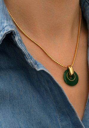 Collier en chaîne dorée avec un pendentif rond vert et un petit anneau entrelacé, posé sur le col d'une chemise en denim.
