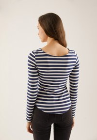 Long-sleeve striped shirt in navy and white, featuring a scoop neckline and a fitted design with a rounded hemline at the back.