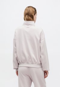 Felpa rosa chiaro con colletto alto e polsini a costine. Tessuto morbido e liscio presenta una vestibilità comoda e un fondo elasticizzato per il massimo comfort.