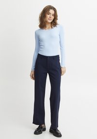 Ljusblå ribbad långärmad topp med en vågig halsringning, i kombination med marinblå vida byxor och svarta loafers.