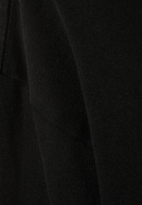 Musta neulottu kangas, jossa on sileä tekstuuri. Kuvassa korostuvat pehmeät laskokset ja saumaton muotoilu lähikuvassa.