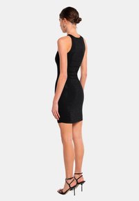 Robe noire ajustée avec une texture côtelée, sans manches, et une longueur au genou. Associée à des escarpins noirs à lanières.