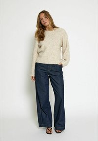 Kremowy, puszysty sweter o luźnym kroju, zestawiony z ciemnoniebieskimi dżinsami o szerokich nogawkach. Oba elementy mają miękką teksturę i casualowy design.