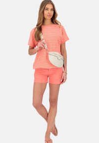 Korálový pruhovaný tričko s krátkymi rukávmi, skombinované s korálovými šortkami. Drží svetlo béžovú crossbody tašku s minimalistickým dizajnom.