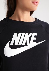 Black sweatshirt featuring a large white Nike logo and swoosh on the front. Made of soft material with a round neckline and raglan sleeves.