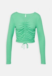 Top corto verde a maniche lunghe con davanti arricciato e coulisse sul bordo, mostrato su uno sfondo bianco semplice.