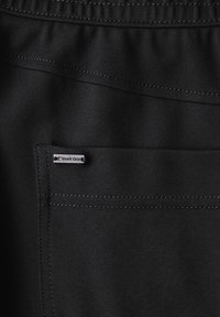 Pohled zblízka na černou látku s našitým kapsou a malou obdélníkovou značkou "Street One" přišitou u okraje kapsy.