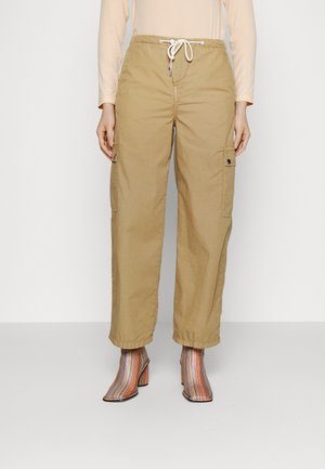 Beige cargo-housut, joissa on naru vyötäröllä ja sivuilla läpällä varustetut taskut, yhdistettyinä raidallisiin korkeakorkoisiin nilkkabootseihin.