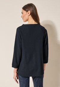Mörkblå blus i en texturerad, veckad tygkvalitet, med trekvartslånga ärmar och rund halsringning, designad för en avslappnad passform.