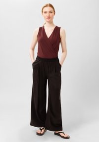 Top senza maniche bordeaux avvolgente abbinato a pantaloni neri a gamba larga; tessuto testurizzato; vita elastica; sandali neri piatti.