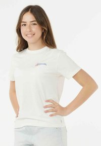 Witte katoenen T-shirt met korte mouwen, voorzien van een blauw en rood logo aan de linkerkant. Het shirt heeft een losse pasvorm en een gladde textuur.