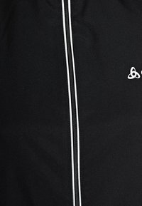 Pantalones deportivos negros de mezcla de algodón con una cremallera lateral blanca en contraste. Presenta un pequeño logo en la parte delantera. Textura suave.
