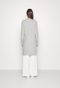 Grauer, längerer Pullover mit gerippter Textur, Rundhalsausschnitt und eng anliegenden Ärmeln, kombiniert mit weißen, weit geschnittenen Hosen. Minimalistisches Design.