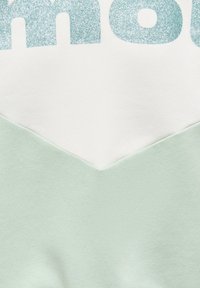 Ανοιχτό πράσινο βαμβακερό φούτερ με λευκό τριγωνικό τμήμα και λαμπερό μπλε κείμενο. Μαλακή υφή, στρωματοποιημένος σχεδιασμός με αντιθετικά χρώματα.