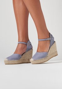 Sandali con zeppa lilla chiaro con tomaia in tela, tacco avvolto in juta e cinturino alla caviglia regolabile. Caratterizzati da punta arrotondata e puntale a contrasto.