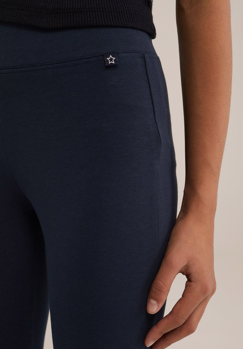 Temno modri, Ujemajoči leggingi z gladko teksturo in majhno zvezdasto oznako na pasu. Prikazane so stranske žepe.
