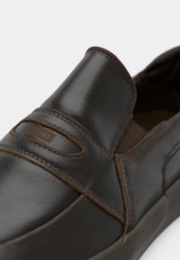 Chaussure à enfiler en cuir marron foncé avec panneaux latéraux élastiques et étiquette "GLOBE" sur le dessus, coutures détaillées et semelle en caoutchouc.