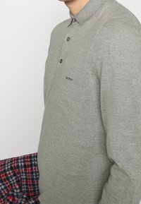 Polo gris en maille avec un col, trois boutons et un petit logo noir sur la poitrine. Tissu texturé.