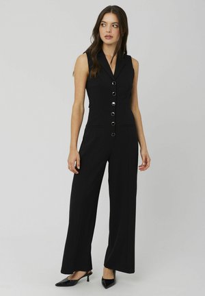 Combinaison noire sans manches avec col, boutons sur le devant, poches latérales et jambes larges, confectionnée dans un tissu lisse et structuré.