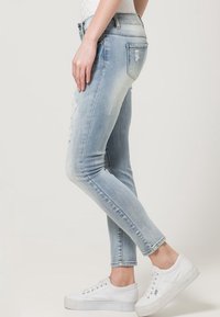 Light blue skinny jeans with distressed accents, standard pockets, and a classic fit, paired with white platform sneakers.